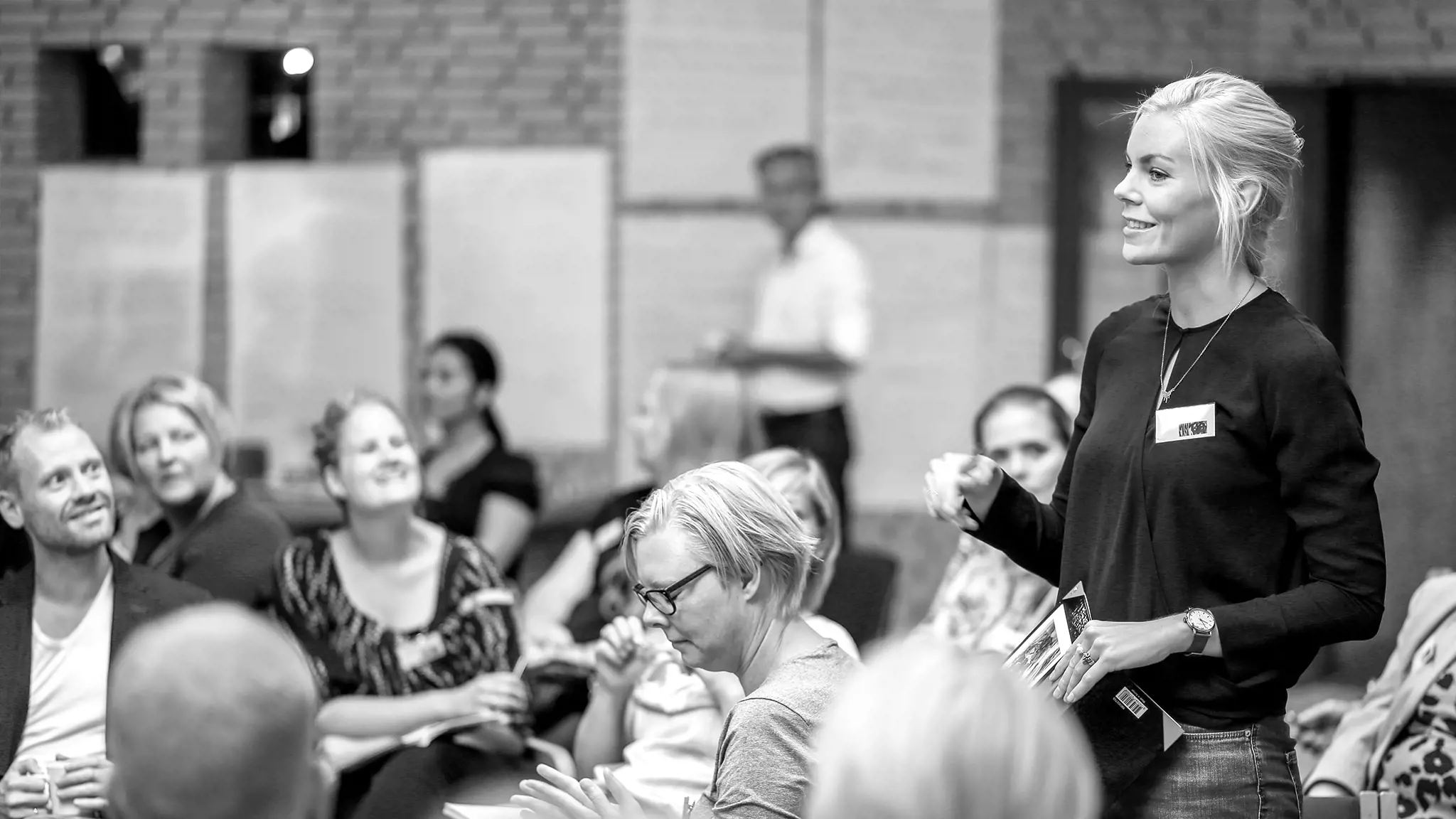 woman standing in an audience speaking with people looking 