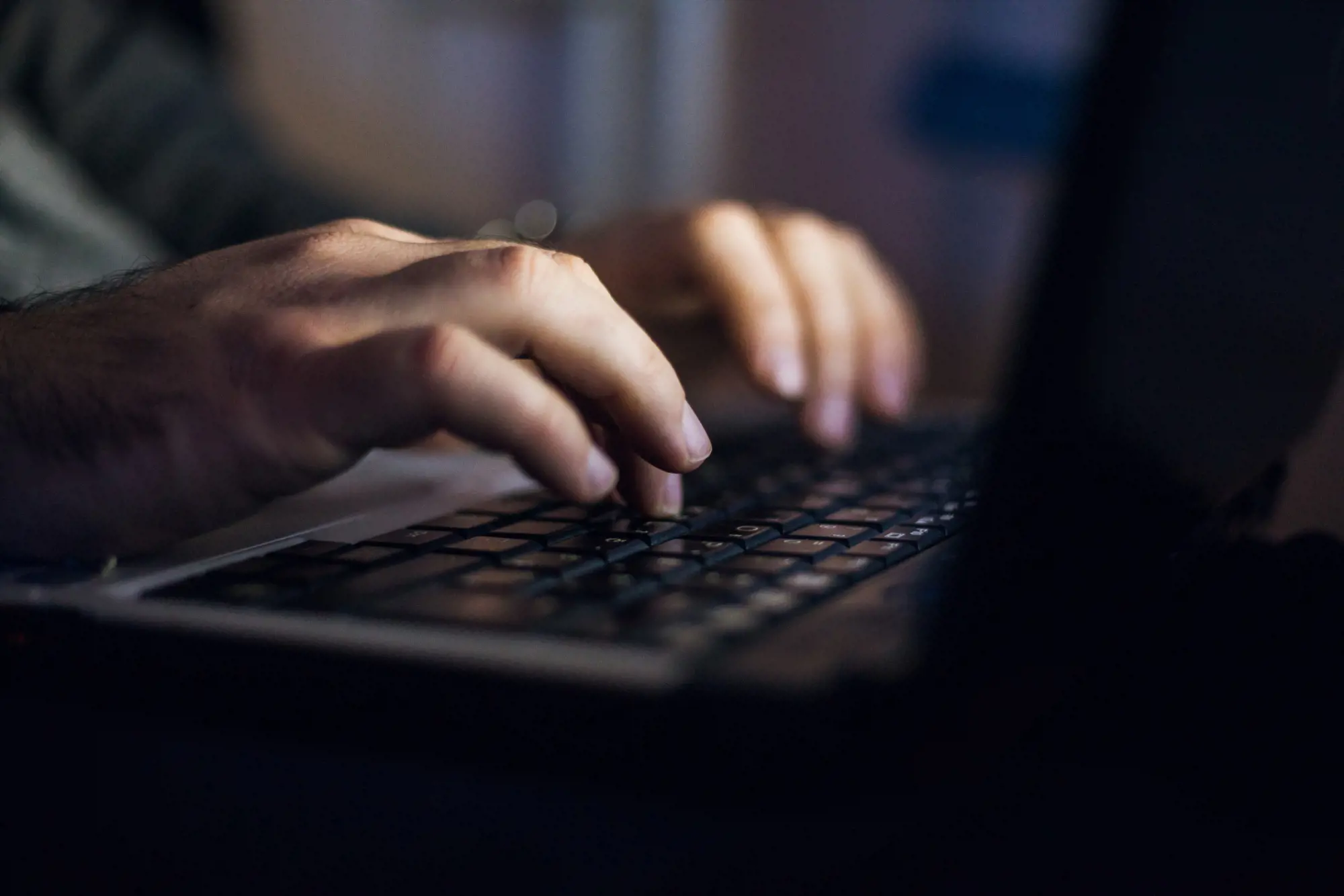 Person taster på bærbar computer i mørkt lokale | Novicell, Digitalt konsulenthus
