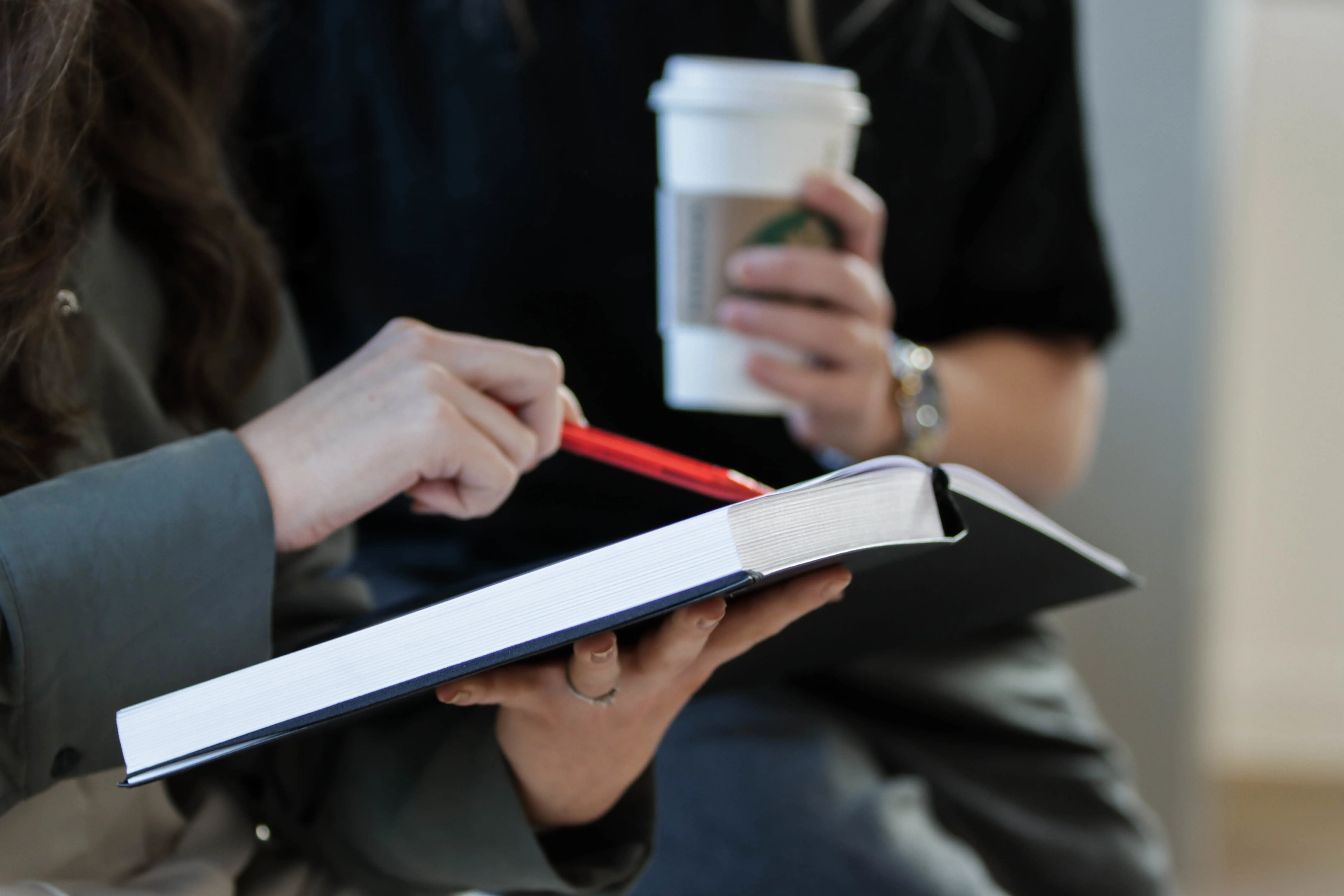woman pointing at a hardcover book and a woman holding a coffee cup in the foreground 