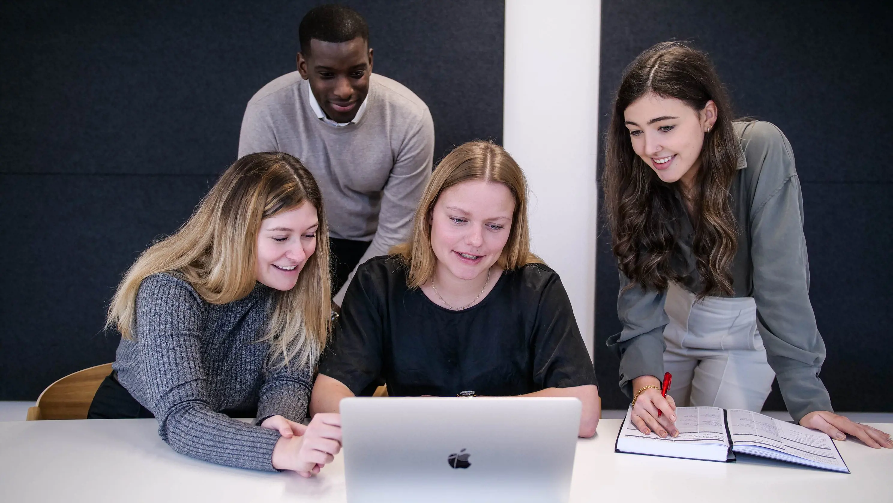 a group of employees gathering around a laptop and engaging in discussion 